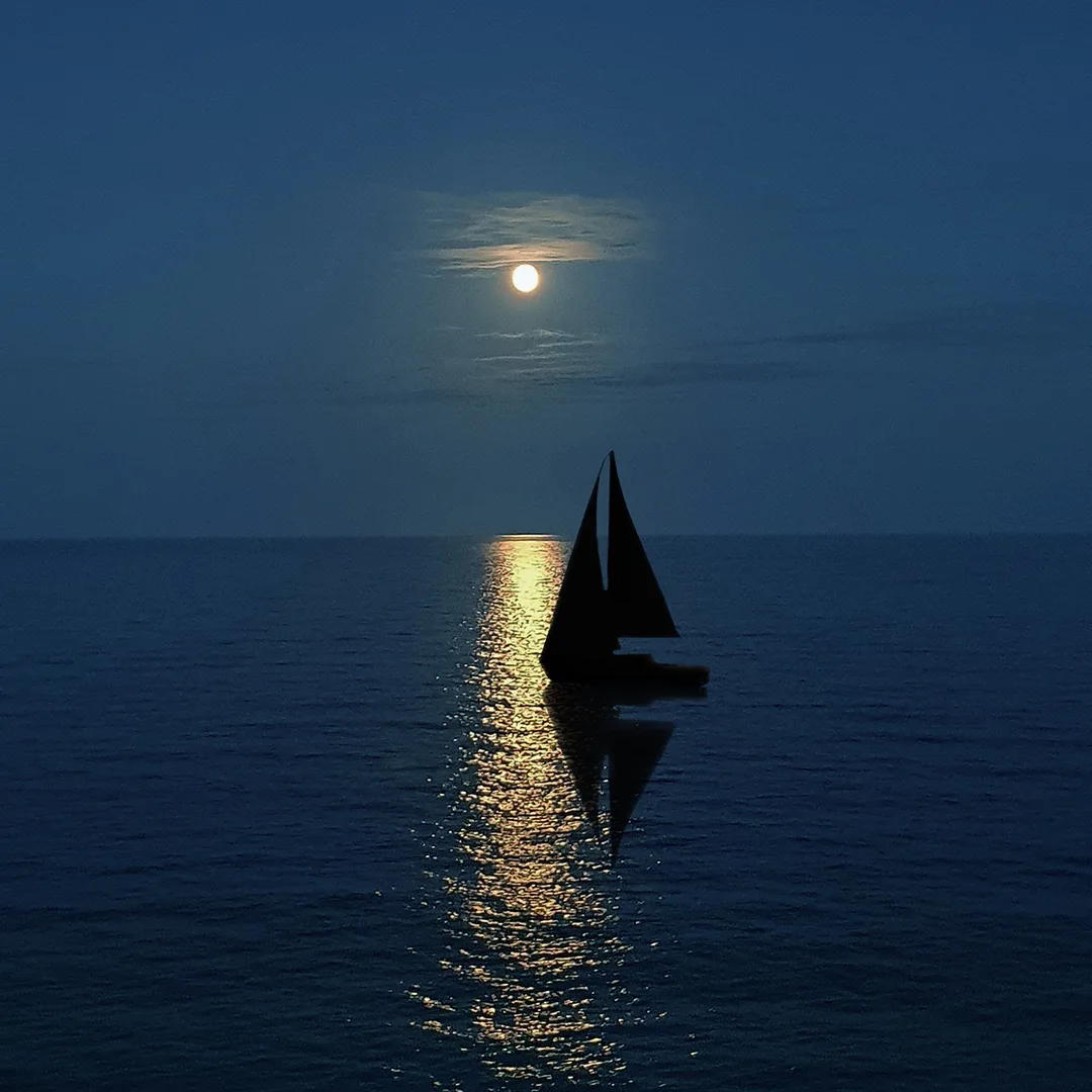 Sailboat sailing into light reflected on a lake by a full moon
